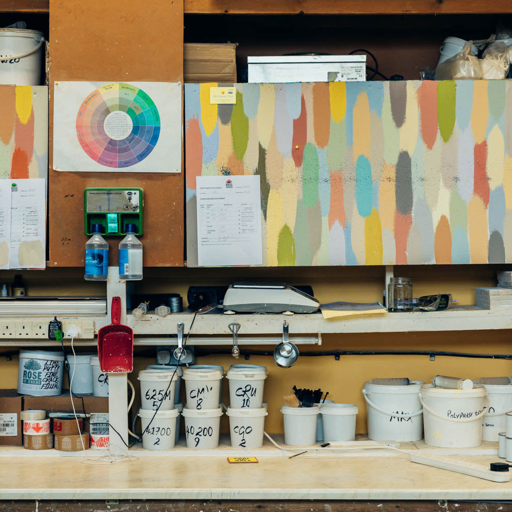 Workshop or studio with paint containers, tools, and color swatches on a wall.