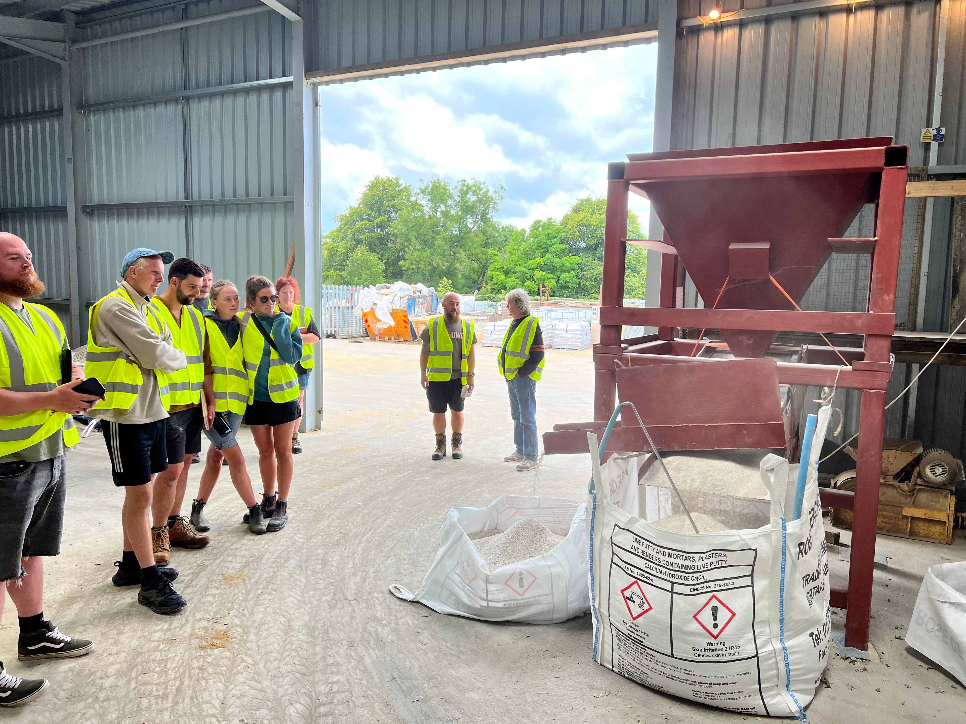 Group of people in safety vests observing a large bag and equipment in a warehouse.